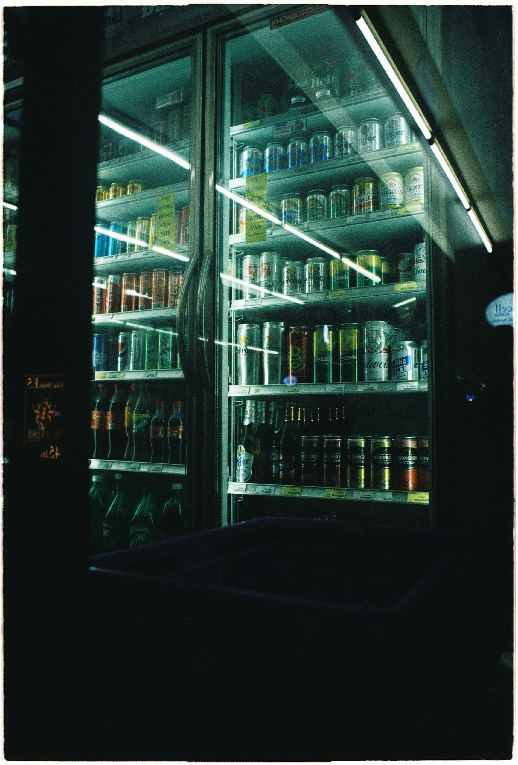 A selection of cans displayed in a brightly lit fridge at night.